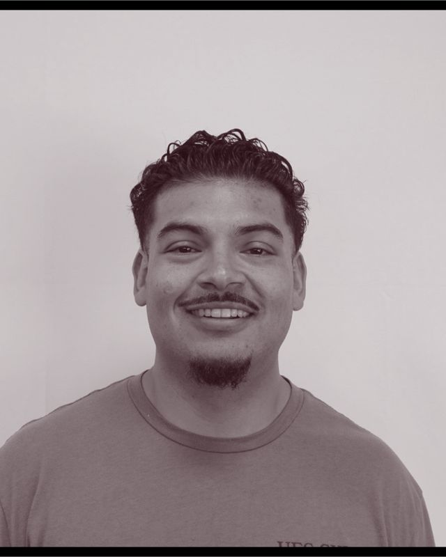 Portrait of barber Edwin “Slick” Flores, smiling, with curly hair and a goatee
