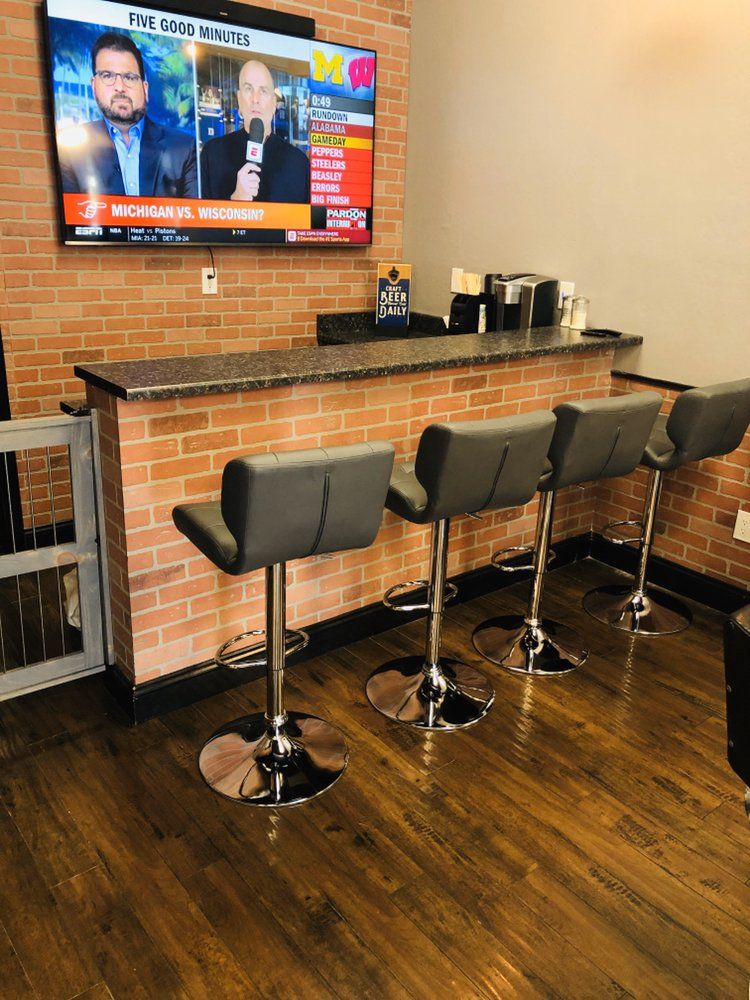 A brick bar counter with four tall stools under a wall TV, a coffee maker on the counter