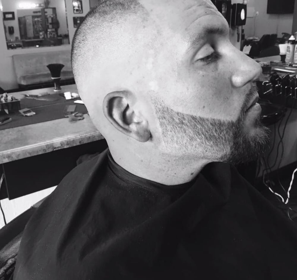 Black and white side profile of a client with a tight skin fade and a sharply lined beard