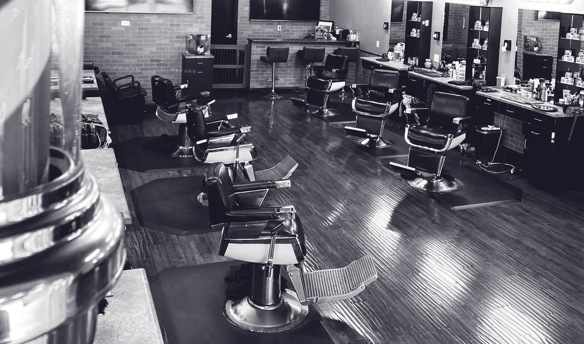 Black and white view down a row of classic barber chairs and stations on a glossy wood floor