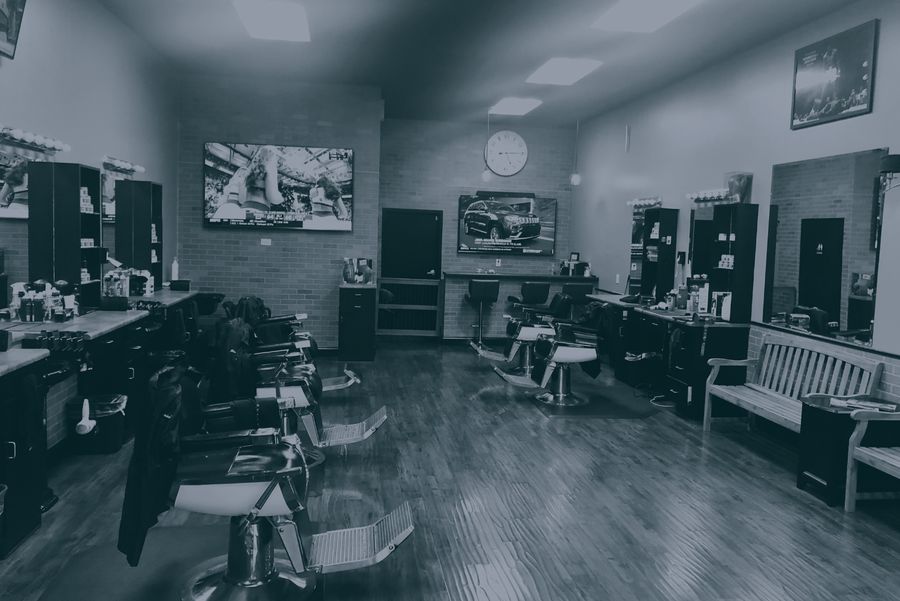 The shop floor: barber chairs down both sides, a brick back wall, a wooden bench and wall-mounted TVs